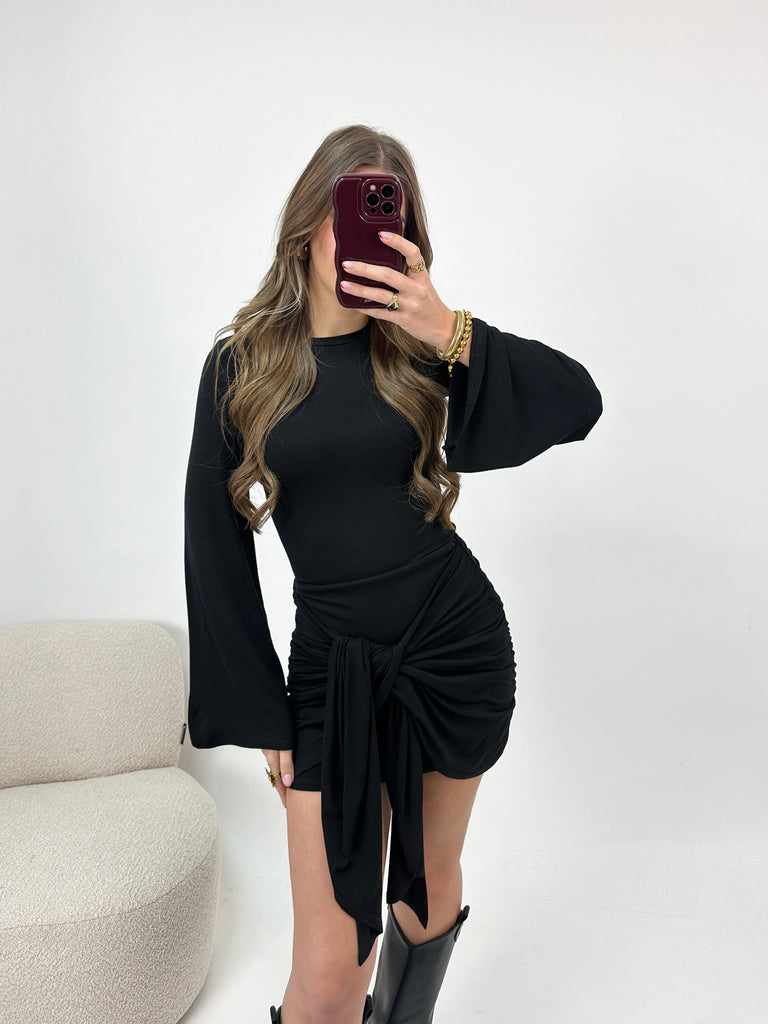Zwart aansluitend jurkje met lange flared mouwen en gedrapeerd effect met knoop aan de voorkant