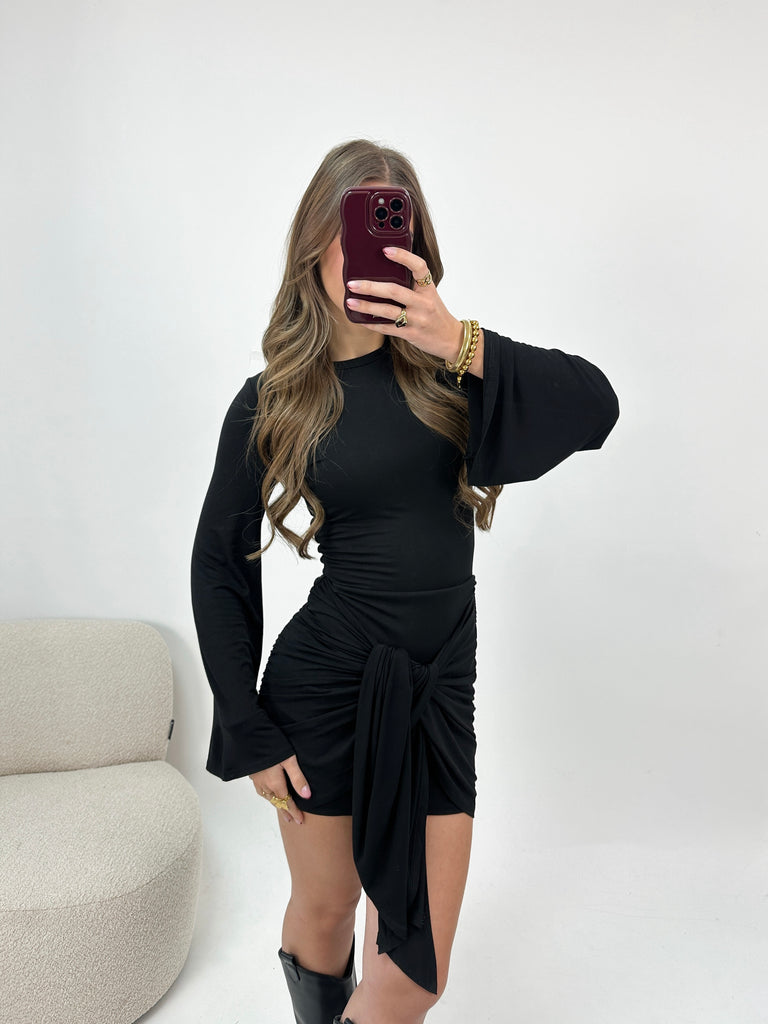 Zwart aansluitend jurkje met lange flared mouwen en gedrapeerd effect met knoop aan de voorkant